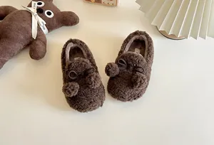 Macro view of brown plush children's slip-on shoes with cute bow and pom pom details.