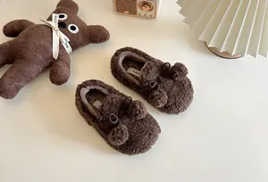 Close-up of cozy brown plush children's loafers with cute pom-pom and bow detail.