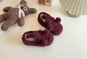 Macro detail of wine red fuzzy children's slip-on shoes with pom-poms in cozy setting