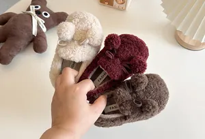 Close-up of plush children's warm slip-on shoes with pom-poms and bows.