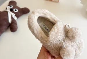 Close-up detail of cozy plush lining and fashion label on children's pom-pom loafers