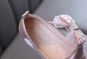 Gros plan de chaussure de princesse rose avec nœud en strass et logo doré sur la semelle