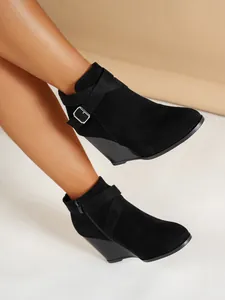 Vue latérale de bottines compensées en daim noir avec boucle portées par un mannequin