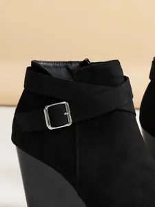 Détail macro d'une bottine en daim noir avec sangle décorative et boucle argentée