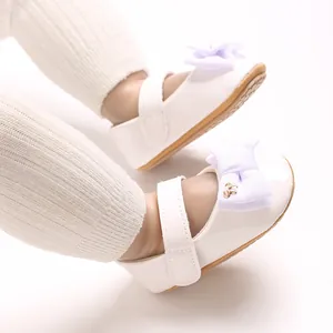 Makrodetail von weißen Baby-Mary-Jane-Schuhen aus Lackleder mit süßen Bandschleifen