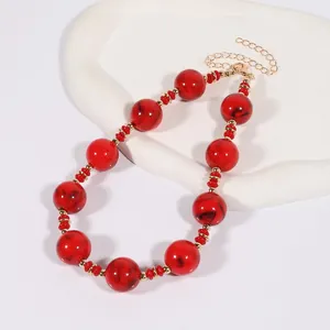 Gros plan d'un collier à grosses perles rouges marbrées avec séparateurs dorés
