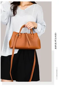 Detail showing a brown pebbled leather tote bag held by a model in a grey sweater