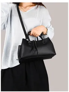 Elegant black pebbled leather tote handbag held by a model in stylish grey sweater.