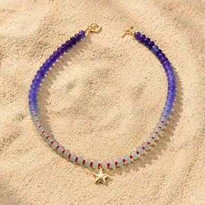 Gedetailleerde weergave van regenboog kralenketting met gouden sterhanger op zand