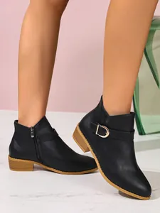 Dettaglio degli stivaletti neri a punta con fibbia dorata e una cerniera laterale.