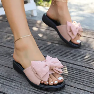 Nahaufnahme einer rosa Stoffschleife auf einer modischen flachen Sandale auf Holz.