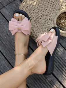 Nahaufnahme von rosafarbenen Damen-Slippers mit großer Zierschleife auf Holzdeck