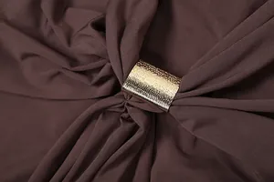 Détail macro d'une boucle métallique dorée sur une robe moulante marron à épaules dénudées.