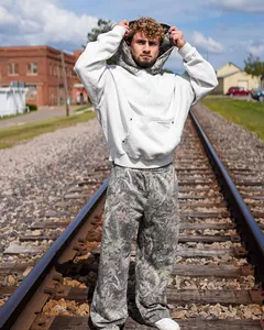 Kaukasisches männliches Model posiert auf Bahngleisen in grauem Hoodie und Camouflage-Hose.