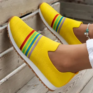 Close-up of yellow breathable fly-knit slip-on sneakers with rainbow stripes.