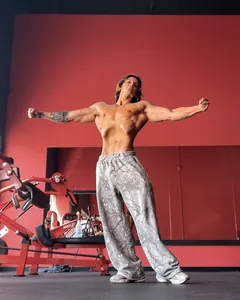 Ganzkörperansicht eines Bodybuilders in lockeren Tarn-Jogginghosen in einem roten Fitnessstudio