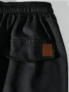 Detail shot of men's black cargo pants featuring elastic waistband and pocket flap