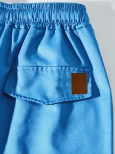 Detail of blue cargo pants featuring an elastic waistband and pocket with leather patch