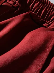 Close-up detail of dark burgundy cargo pants fabric showing elastic waistband texture.