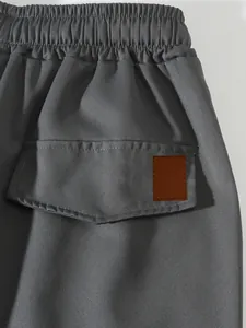 Detail shot of men's grey cargo pants featuring elastic waistband and leather patch
