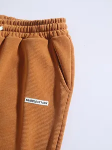 Detail of men's brown corduroy pants showing fabric texture and MUSCLEATTACK label