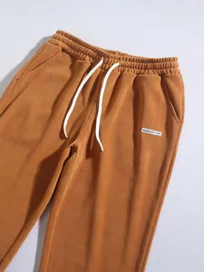 Close-up of ginger corduroy pants featuring white drawstrings and logo patch detail