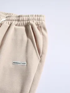 Close-up detail of beige corduroy men's pants featuring a woven logo and elastic waist