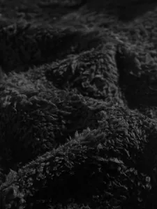 High-quality macro view of black fuzzy faux fur fabric showing soft material texture.
