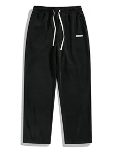 Detailed view of black corduroy men's trousers with white drawstring and logo label.