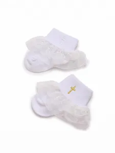 Close-up of white baby socks with delicate lace ruffles and gold cross embroidery.