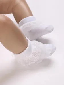 Detailed view of white infant socks with delicate lace ruffles and cross embroidery