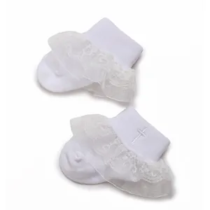 Detail of white baby socks featuring delicate lace ruffles and embroidered cross pattern.
