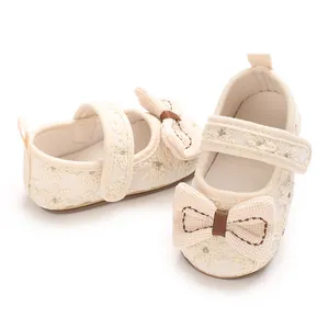 Detailansicht der zarten Stickerei und Schleife auf beigen Baby-Prinzessin-Schuhen.