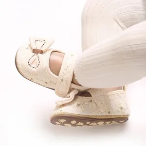 Nahaufnahme von cremefarbenen Baby-Prinzessinenschuhen mit floraler Stickerei und Schleife.