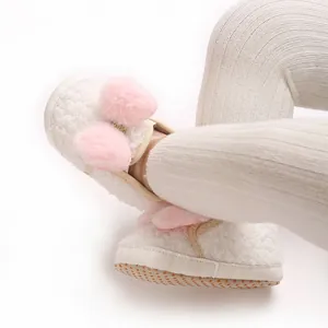 Close-up view of white fuzzy baby pre-walker shoes featuring pink pom-poms and anti-slip soles