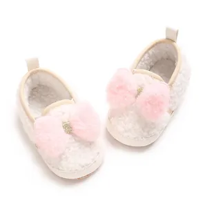 Detail view of plush white baby shoes with decorative pink faux fur pom-pom bows