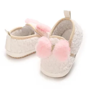Close-up of cute fluffy white baby girl crib shoes with soft pink plush bow decoration
