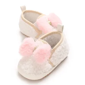 Close-up of white fuzzy baby crib shoes with large pink fur bow details