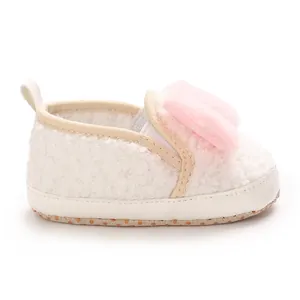 Close-up of white fluffy baby girl crib shoe with soft sole and pink pom-pom detail