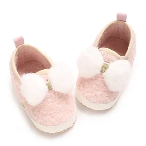 Adorable pink fuzzy baby girl crib shoes with white pom-pom bows and soft soles