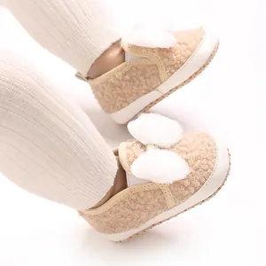 Close-up of soft beige baby shoes with fluffy white pom-poms for girls.