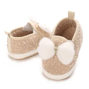 Close-up of beige fleece baby girl crib shoes with fluffy white bow detail