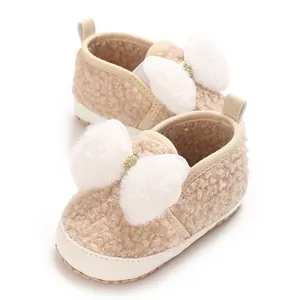 Close-up of fuzzy baby girl crib shoes with soft white plush bow detailing and cream texture.