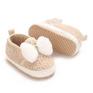 Cute beige fuzzy infant crib shoes with plush white bow and non-slip soft sole detail
