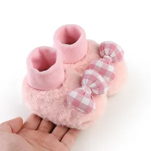Detailed close-up view of soft pink fuzzy baby booties with a plaid bow for newborns.