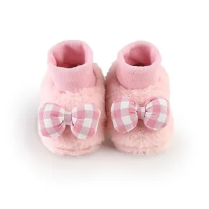 Close-up of pink fuzzy winter baby sock shoes with checkered bow accents for newborns