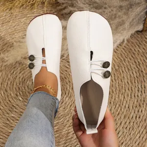 Close-up of white soft leather slip-on shoes with textured finish and button detail.