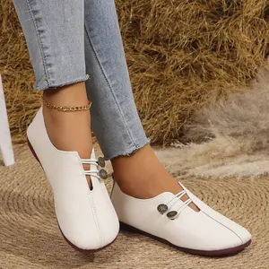 Primer plano de mocasines blancos de cuero suave con correas elásticas y botones decorativos.