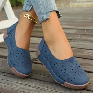 Detalle de los zapatos planos azules con flores caladas para mujer sobre madera