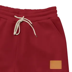 Vista detallada de pantalones deportivos rojos para hombre con cordón y parche de cuero.